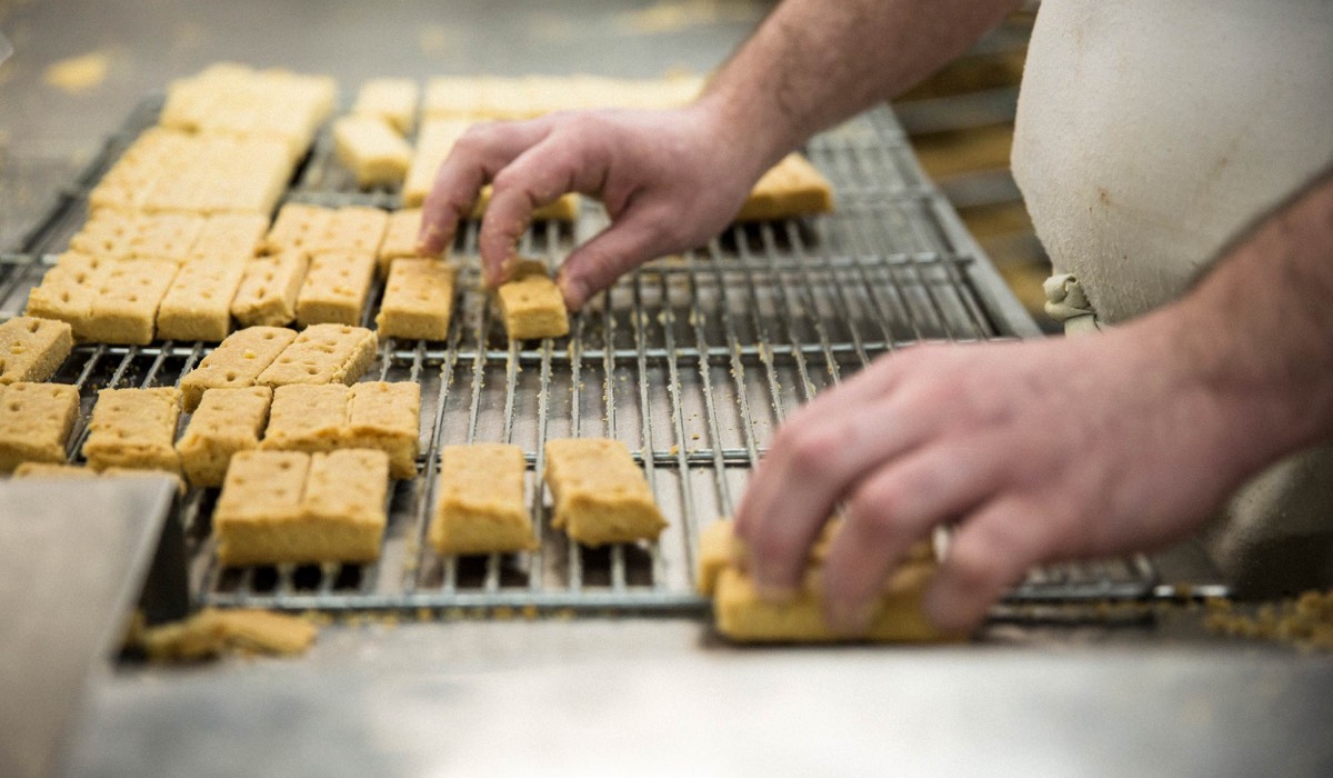A man taking bars of shortbread off a rack in a kitchen