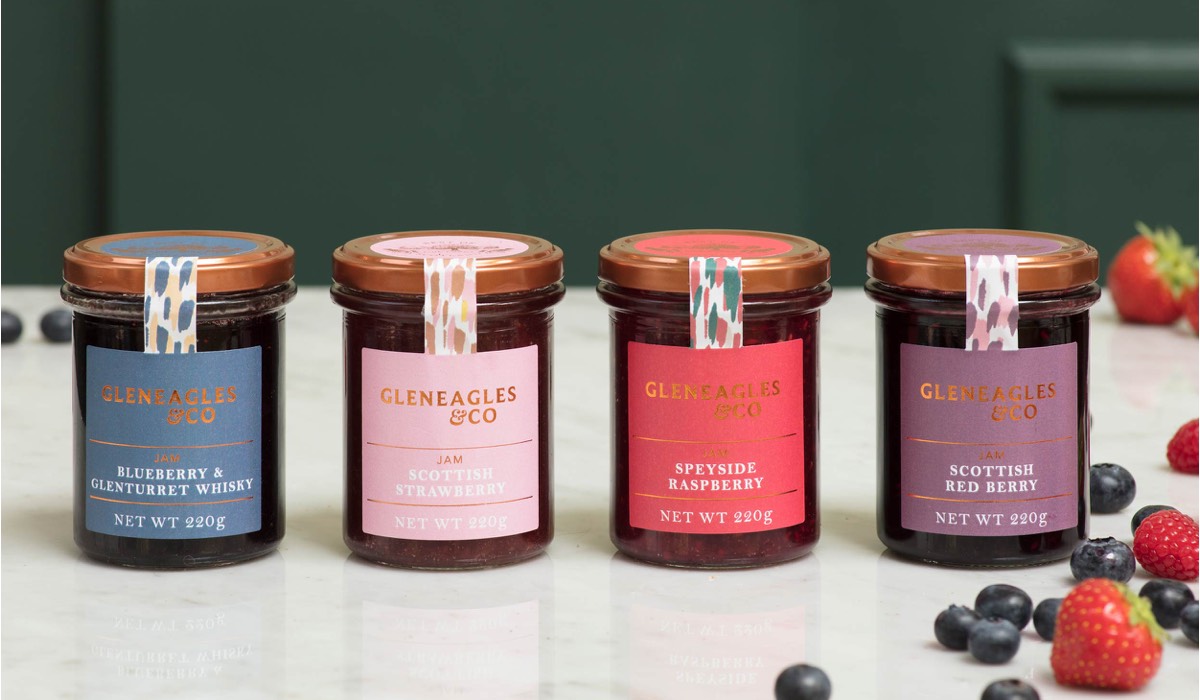 Four jam jars in a row surrounded by soft fruits