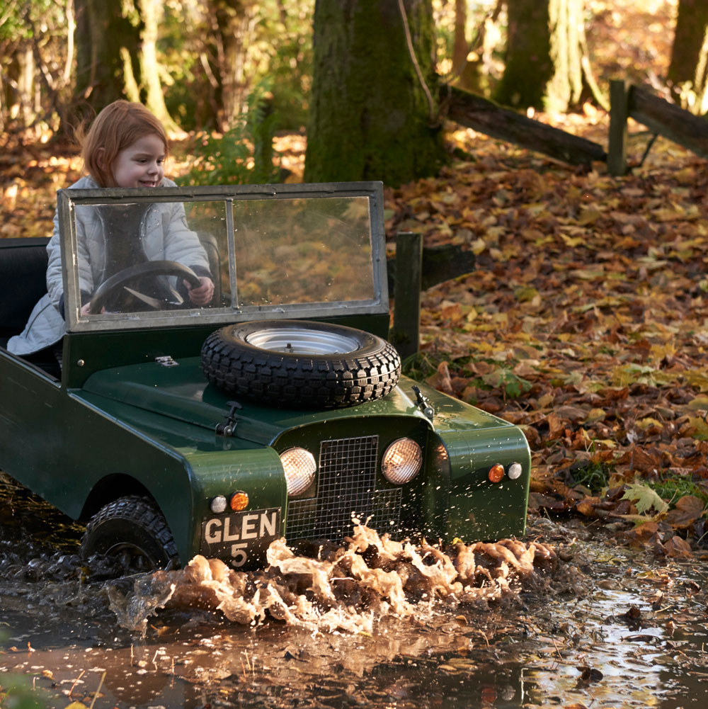 A young girl drives a mini Land Rover through a water feature