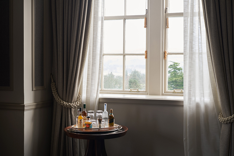 A selection of premium spirits sit on a mahogany table in front of a large brightly lit window