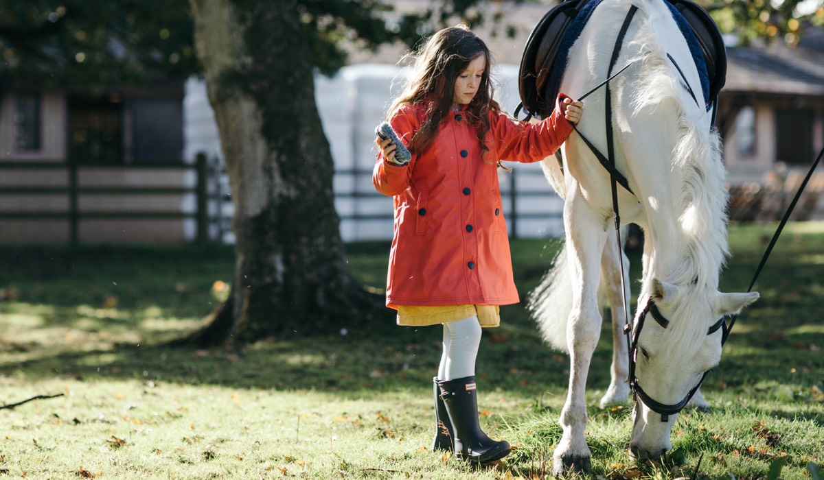 A young girl in a red jacket pats her pony
