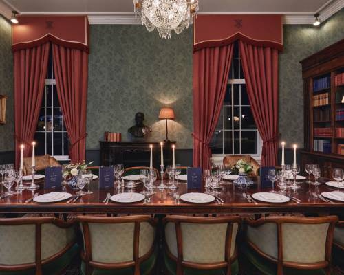 A large mahogany table laid for dinner with silver cutlery and candelabras