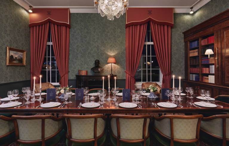 A large mahogany table laid for dinner with silver cutlery and candelabras