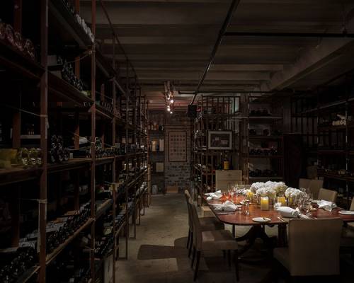 Long wine racks with hundreds of bottles of wine surround an intimate table set for 8 in the atmospheric cellars