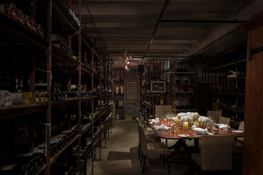 Long wine racks with hundreds of bottles of wine surround an intimate table set for 8 in the atmospheric cellars