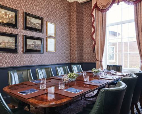 The study, set up for a boardroom meeting with large mahogany table, 10 green leather chairs and pads and pens on the table