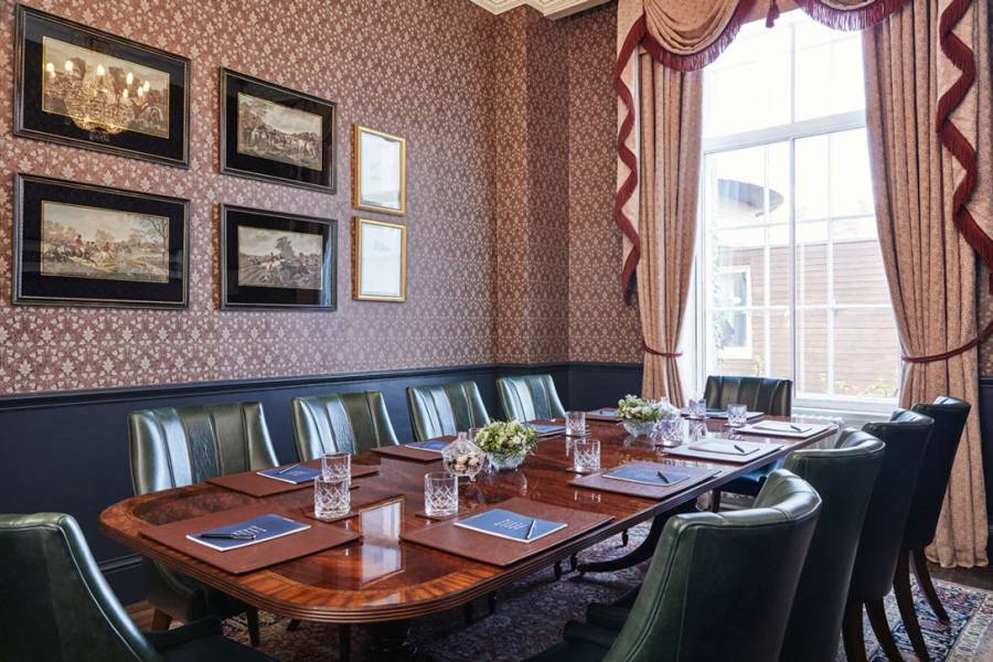 The study, set up for a boardroom meeting with large mahogany table, 10 green leather chairs and pads and pens on the table