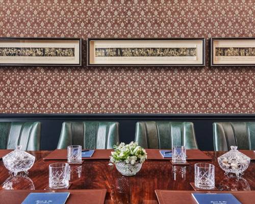 Four green leather chair sit next to a large table set up for a board meeting