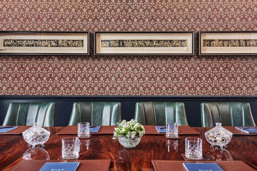 Four green leather chair sit next to a large table set up for a board meeting