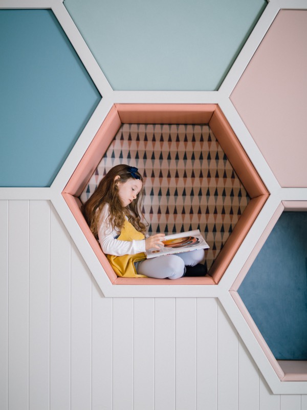 A girl reads a book in a hexagonal cubby hole seat in The Den