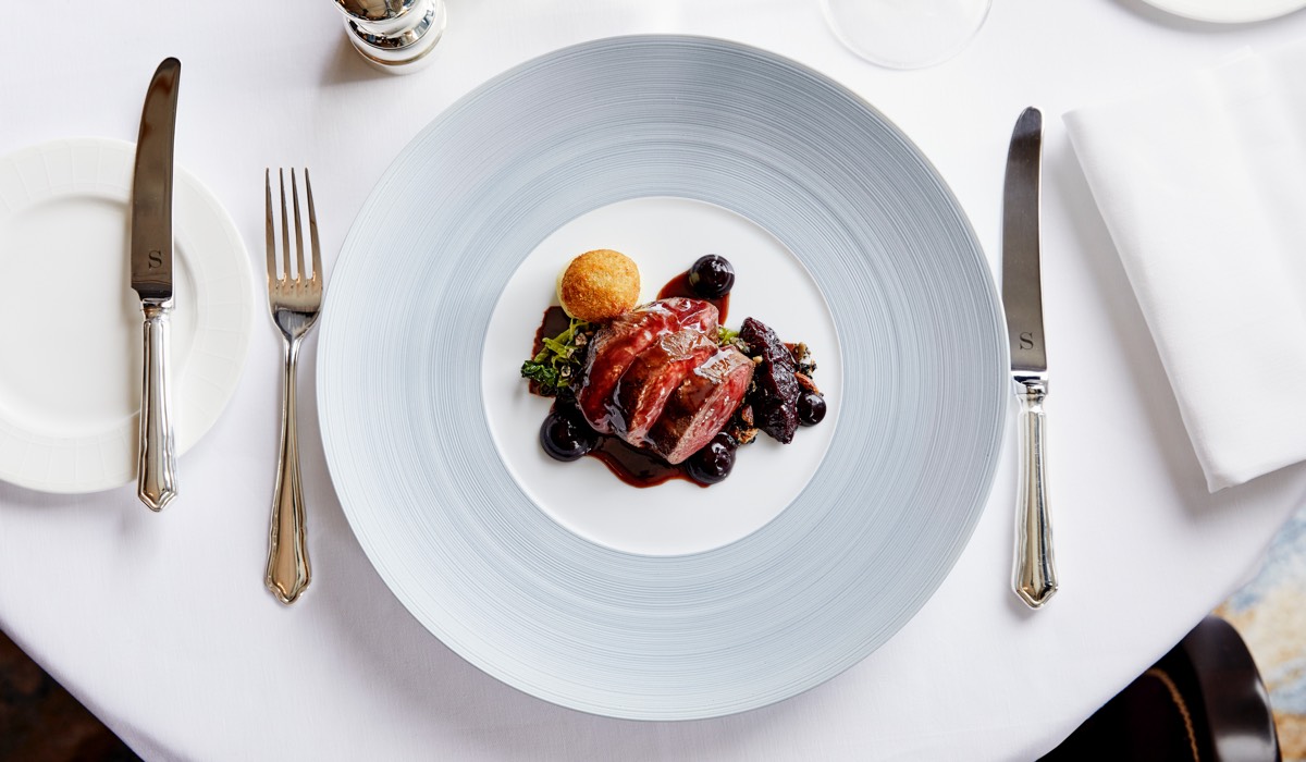 Rare beef on a reduction sauce with a breaded bon bon on a white plate