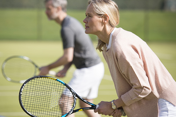 A woman poises fto return a serve on an outdoor tennis court