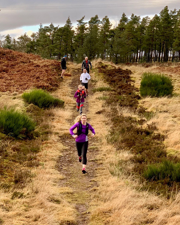 A group of trail runners run down a hill over a moor at gleneagles