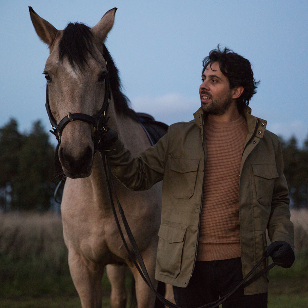 A man walks a grey horse on lead rein at dusk