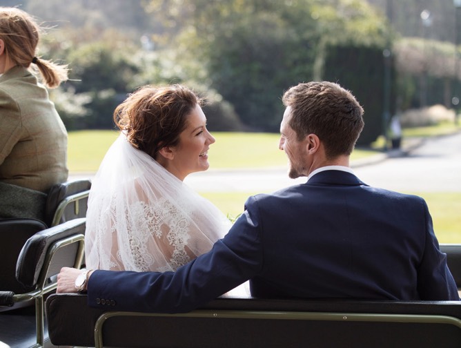 A bride and groom look in each others eyes on the back of a horse drawn carriage