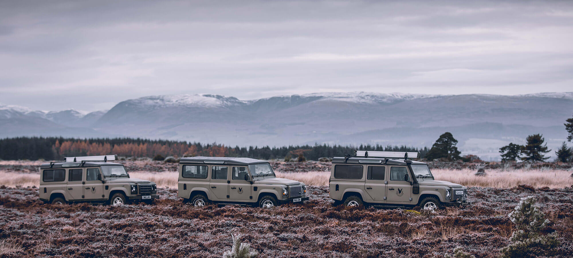 Three Land Rover Defenders in front of snowy mountains near Gleneagles