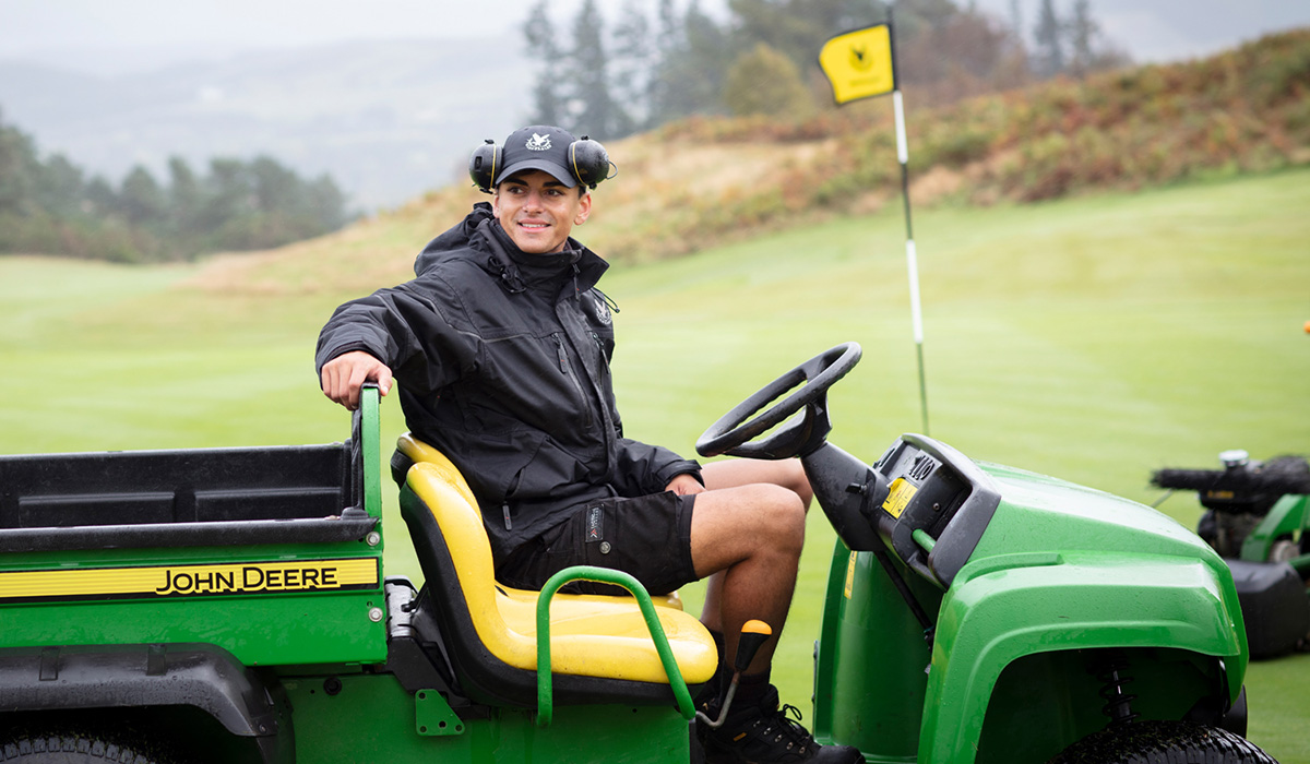 An apprentice Greenkeeper on a lawnmower