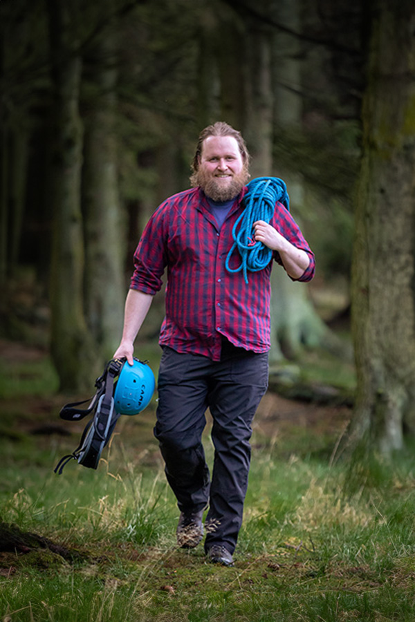 A man walking toward the camera a with climbing helmet and ropes
