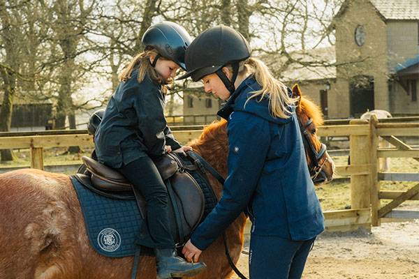 Young woman helping young girl on horse riding lesson at Gleneagles