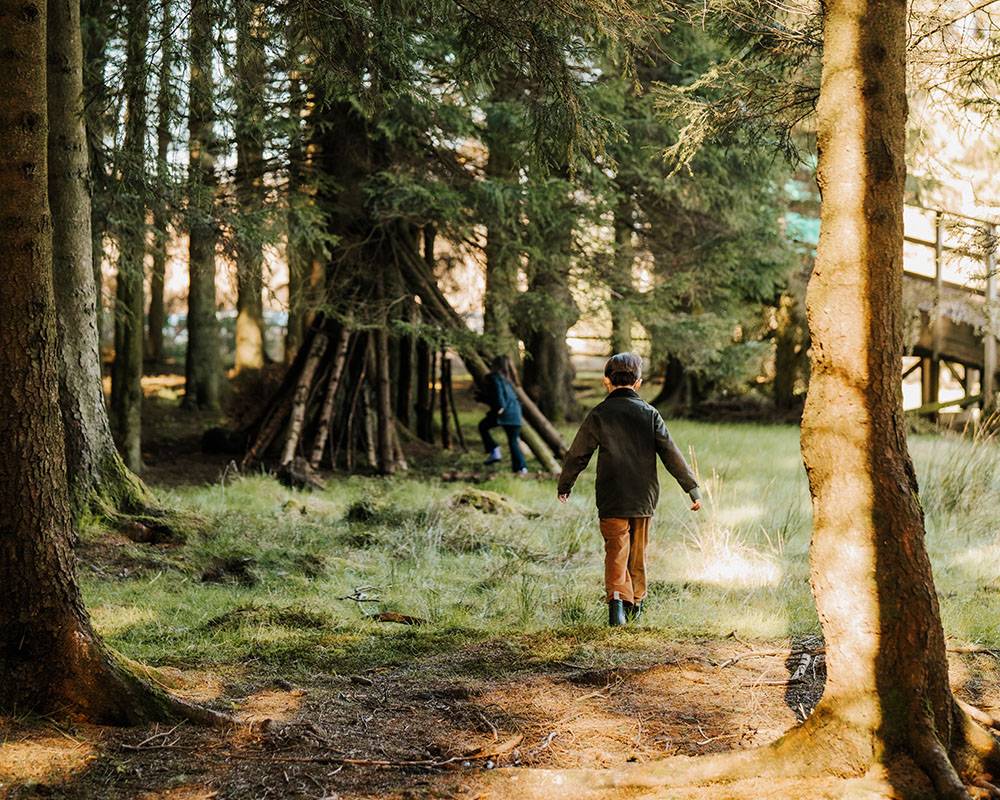 Boy and girl walk in woodland area at Gleneagles, sun shining on trees